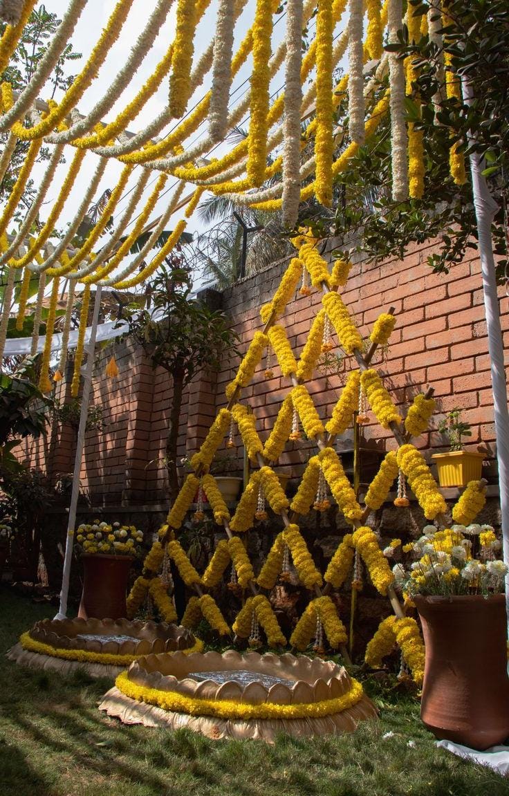 Haldi setup with a marigold garland canopy, yellow drapes and terracotta pots by RAW Group